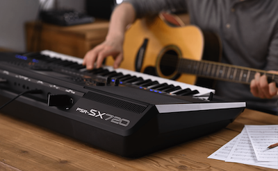 Photo of a person playing Yamaha Arranger Workstation PSR-SX720 while holding a guitar